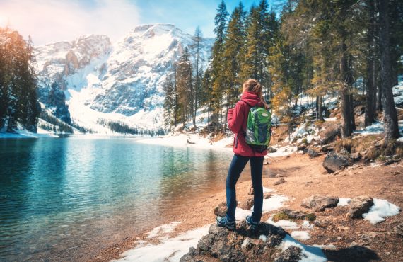 woman with backpack on the stone near lake with azure water