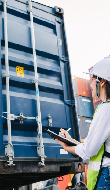 Asian staff woman checking container box for logistic Import Export in dock